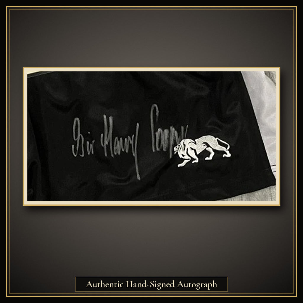 Close-up of Sir Henry Cooper's silver marker signature on the lower front leg of the Lonsdale boxing shorts, beside the Lonsdale lion logo